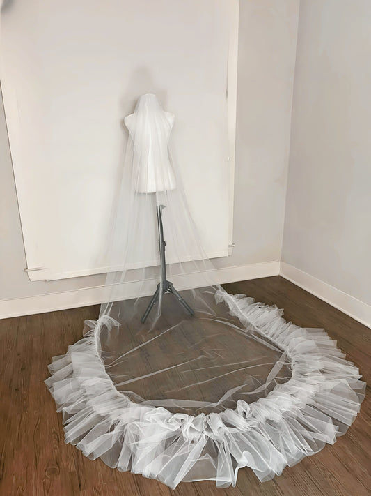 A dramatic cathedral wedding veil with voluminous ruffled layers displayed on a mannequin.