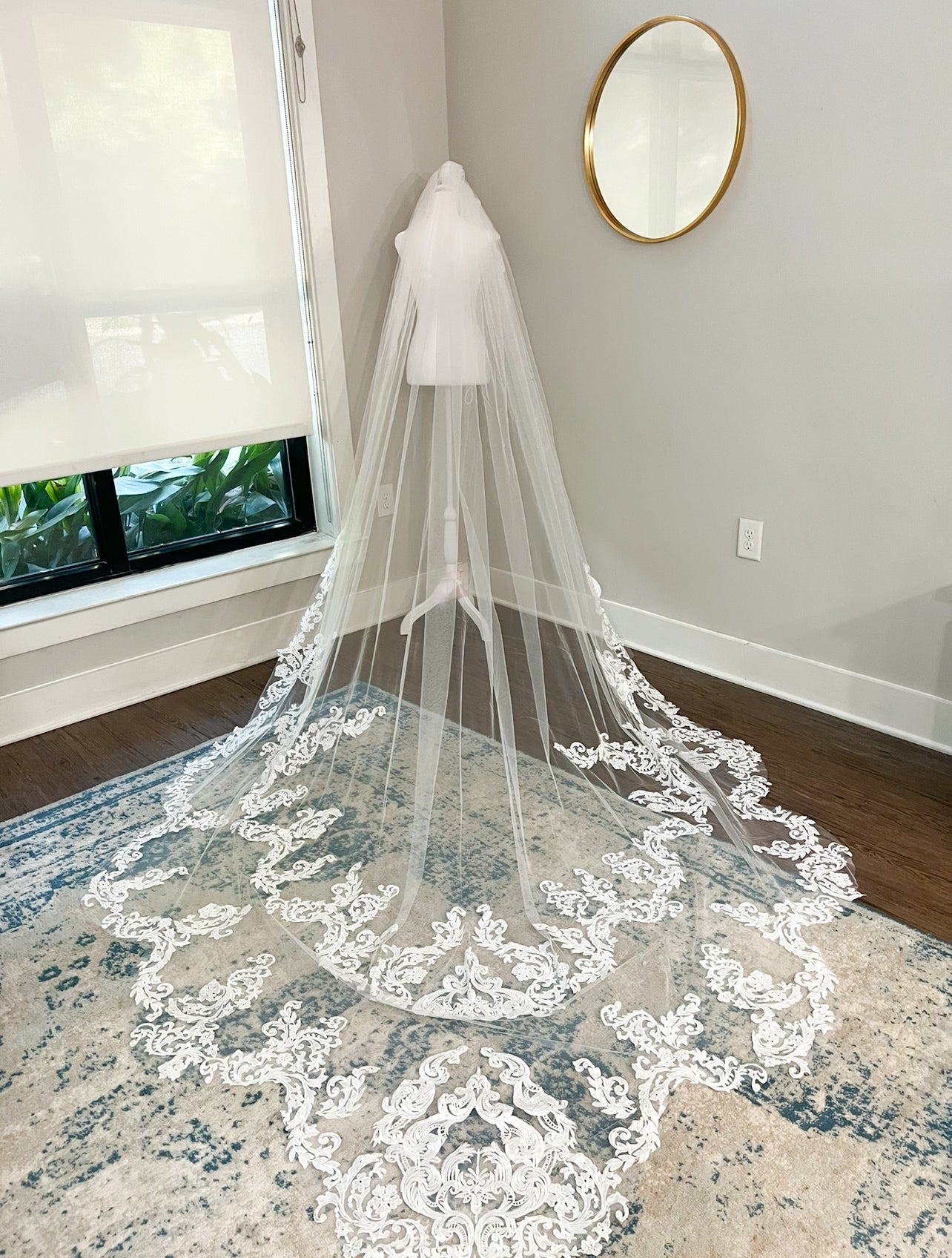 Cathedral-length wedding veil with intricate floral lace embroidery displayed on a white mannequin in a bridal studio.