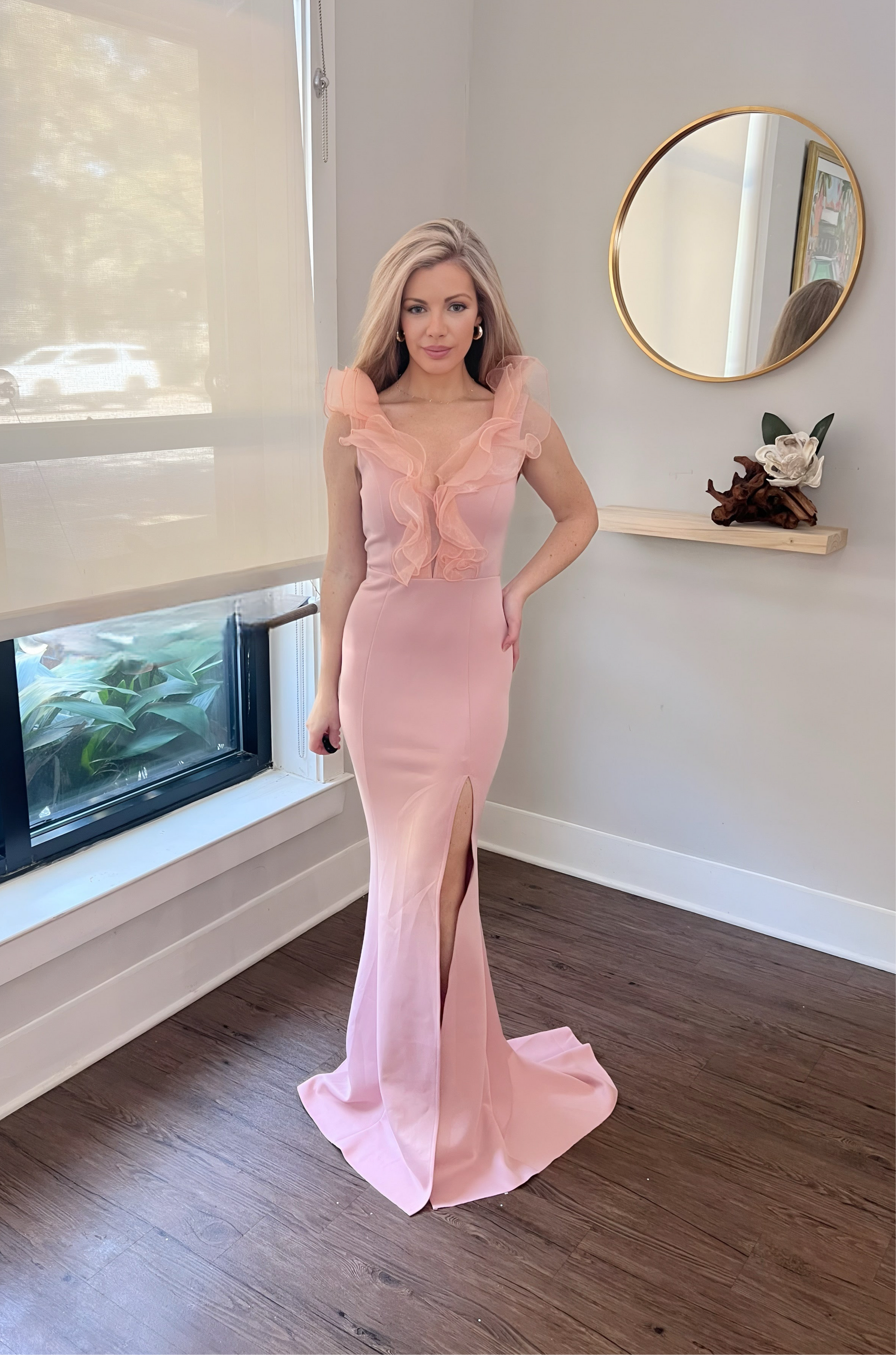 A woman in a pink formal dress with a deep V-neckline and ruffled detailing, featuring a thigh-high slit.