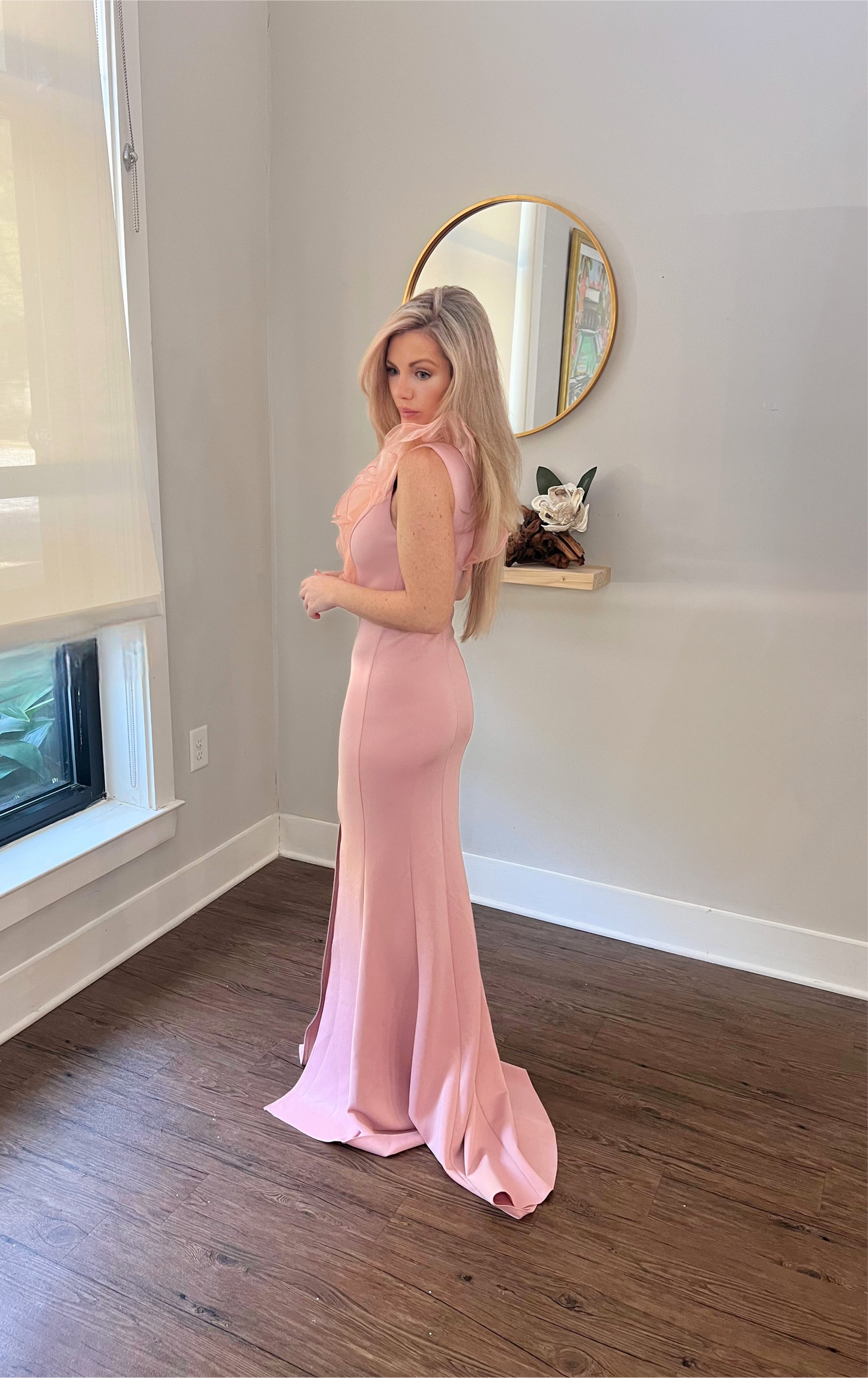 A woman turned slightly in a pink formal dress with a deep V-neckline and ruffled detailing, featuring a thigh-high slit.