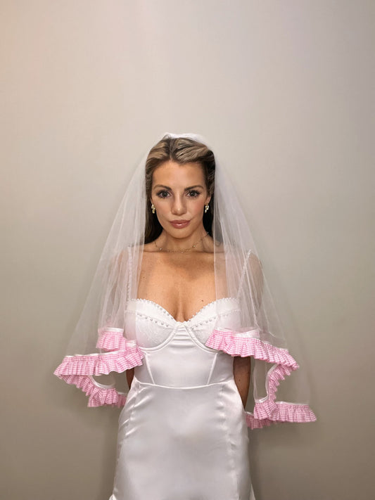 A woman wearing a white bridal gown and a pink ruffle trim wedding veil.
