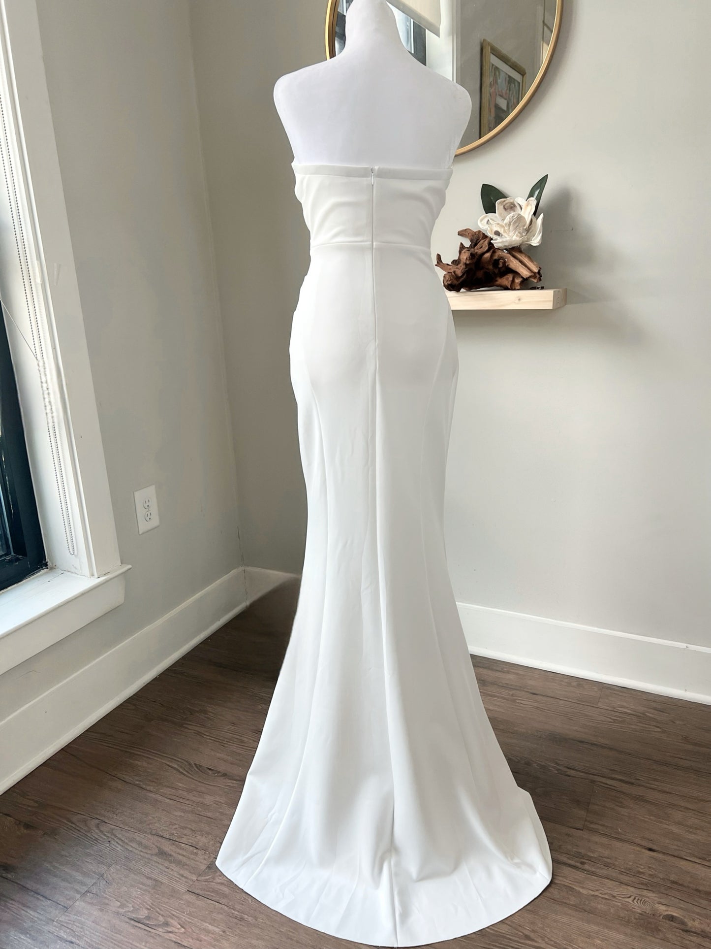 Back view of a strapless mermaid wedding dress showcasing the fitted silhouette and elegant train on a white mannequin.